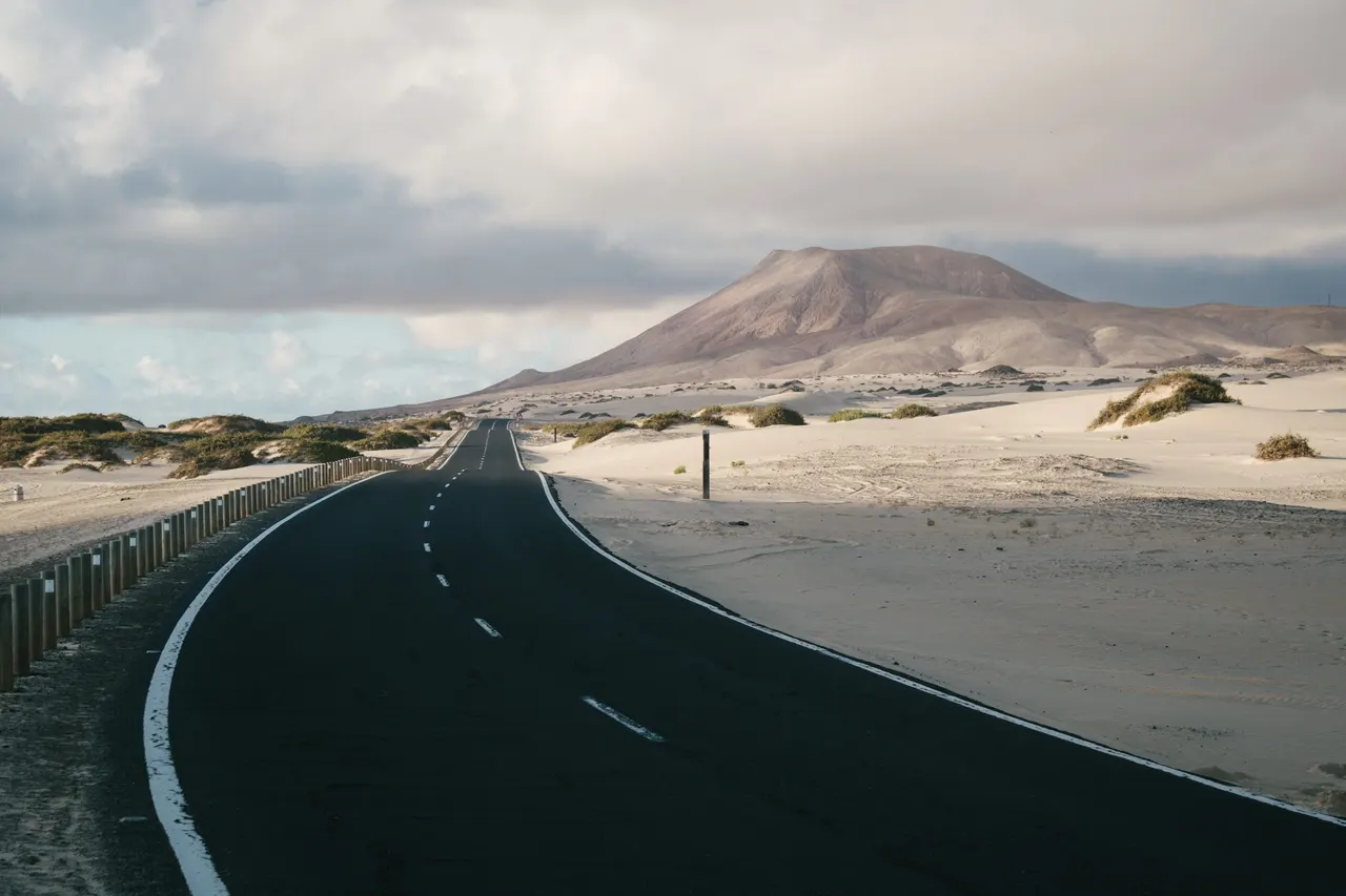 Straße durch Sand- und Vulkanlandschaft auf Fuerteventura
